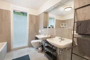 A modern bathroom with a toilet, two sinks, a shower, and a large mirror.