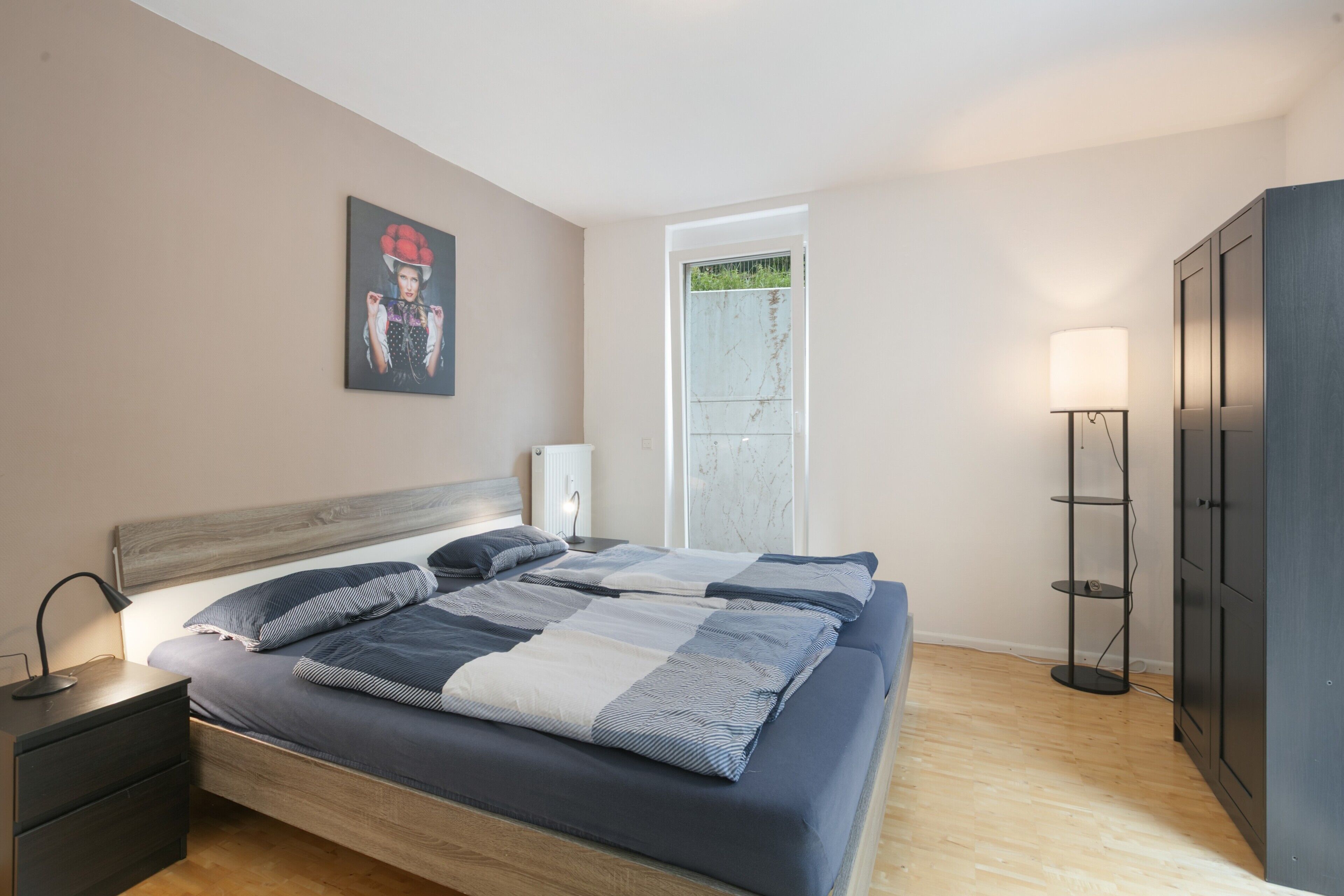 A bedroom with a bed, bedside table, lamp, wardrobe, and a door leading to a balcony.