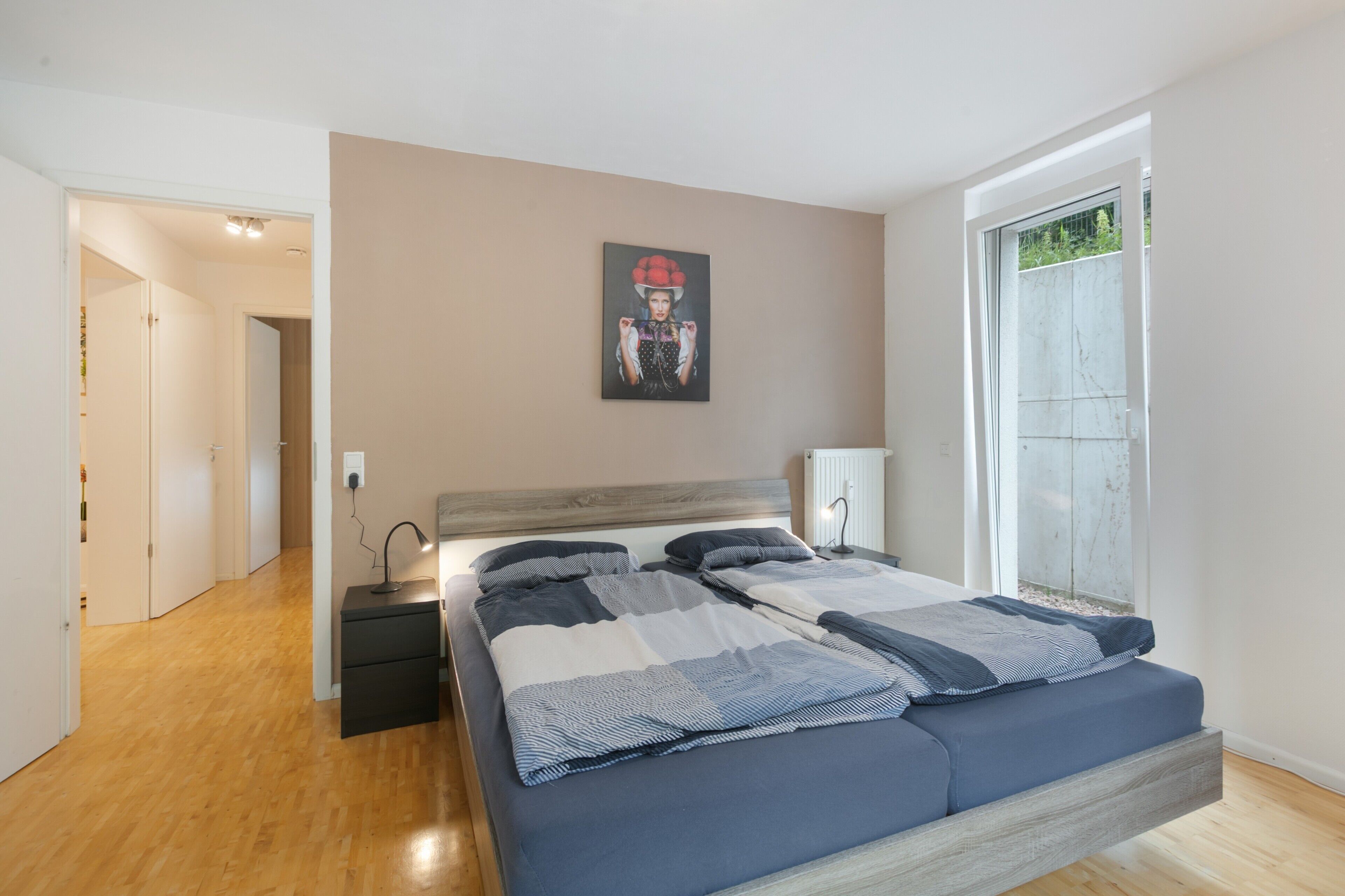 Ein Schlafzimmer mit einem Bett, Nachttischen, einer Wandlampe und einem Fenster.