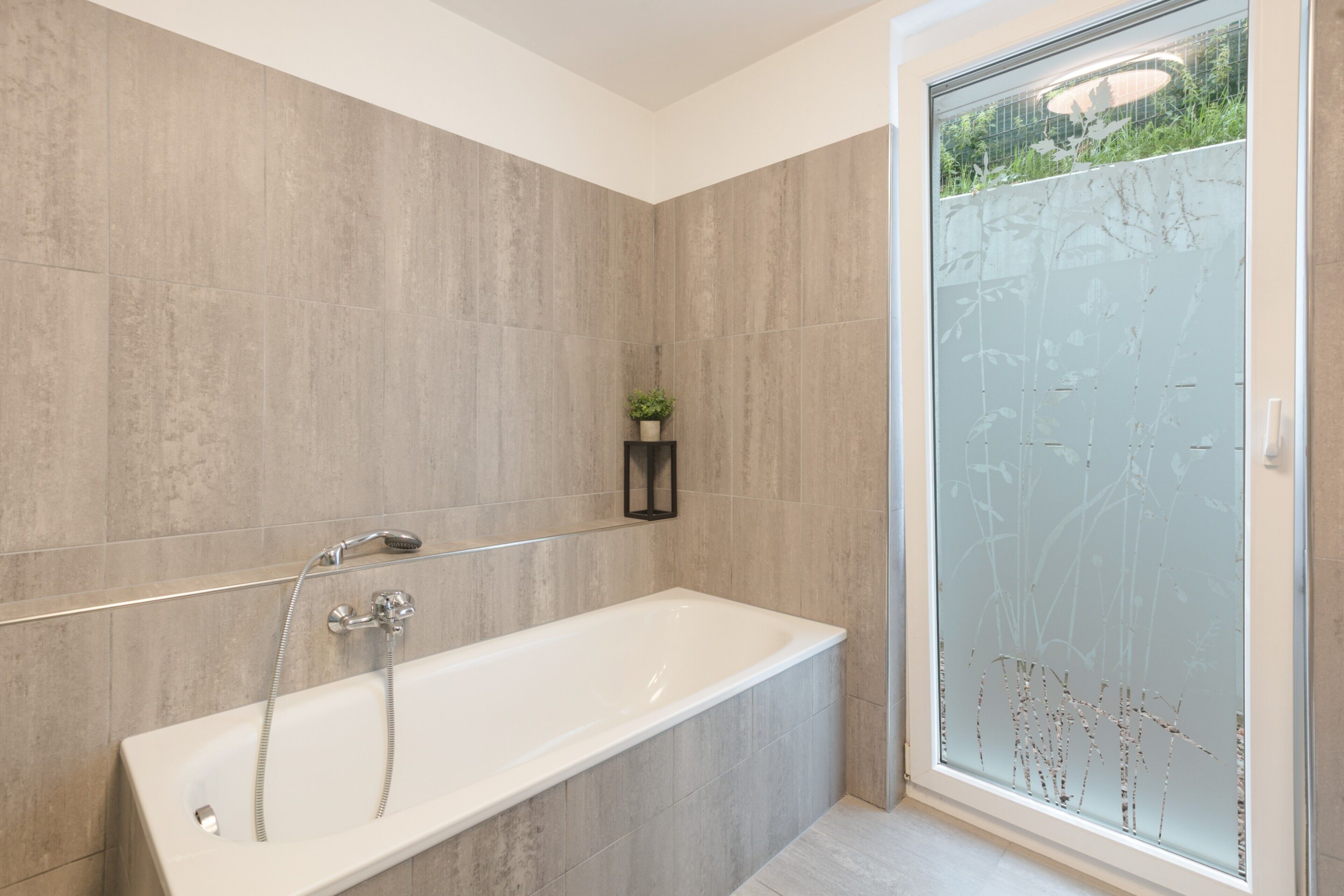 Ein modernes Badezimmer mit einer freistehenden Badewanne, einer Duschkabine aus Glas und einem kleinen Topfpflanzen auf einem Regal.