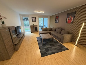 Ein modernes Wohnzimmer mit einer Couch, einem Couchtisch, einem Fernseher und einer Zimmerpflanze.