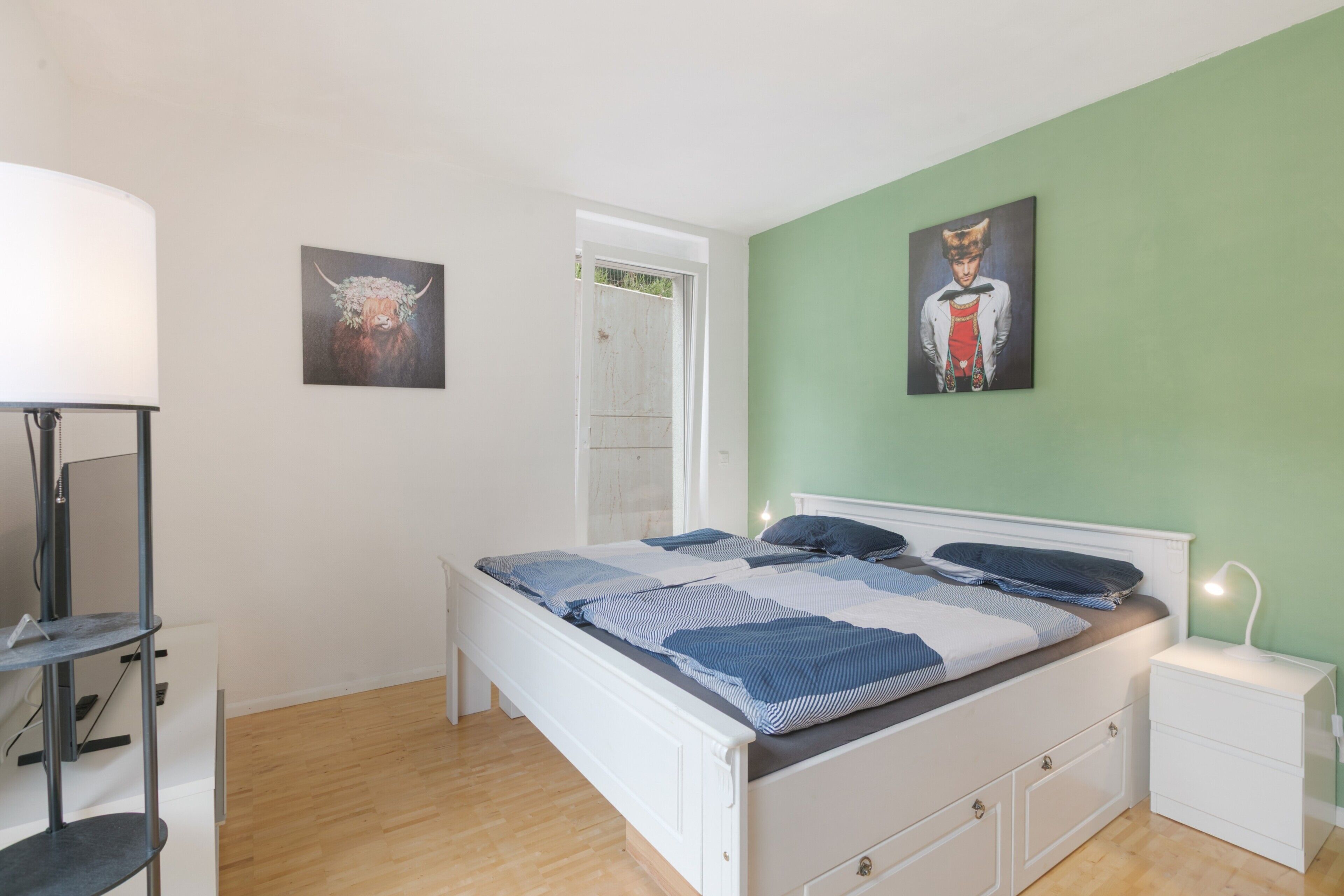 Quarto com cama, mesas de cabeceira, guarda-roupa e duas imagens penduradas na parede.