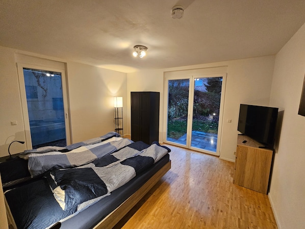Ein Schlafzimmer mit einem Bett, einem Fernseher, einer Lampe und einer Glastür zum Außenbereich.