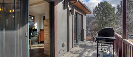 A covered deck with a barbecue grill and propane tank, a sliding glass door leading to an interior with a kitchen and seating area.