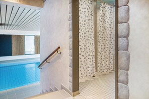 Une piscine dotée d’une rambarde en bois, d’un sol carrelé et d’un espace douche agrémenté de rideaux à motifs.