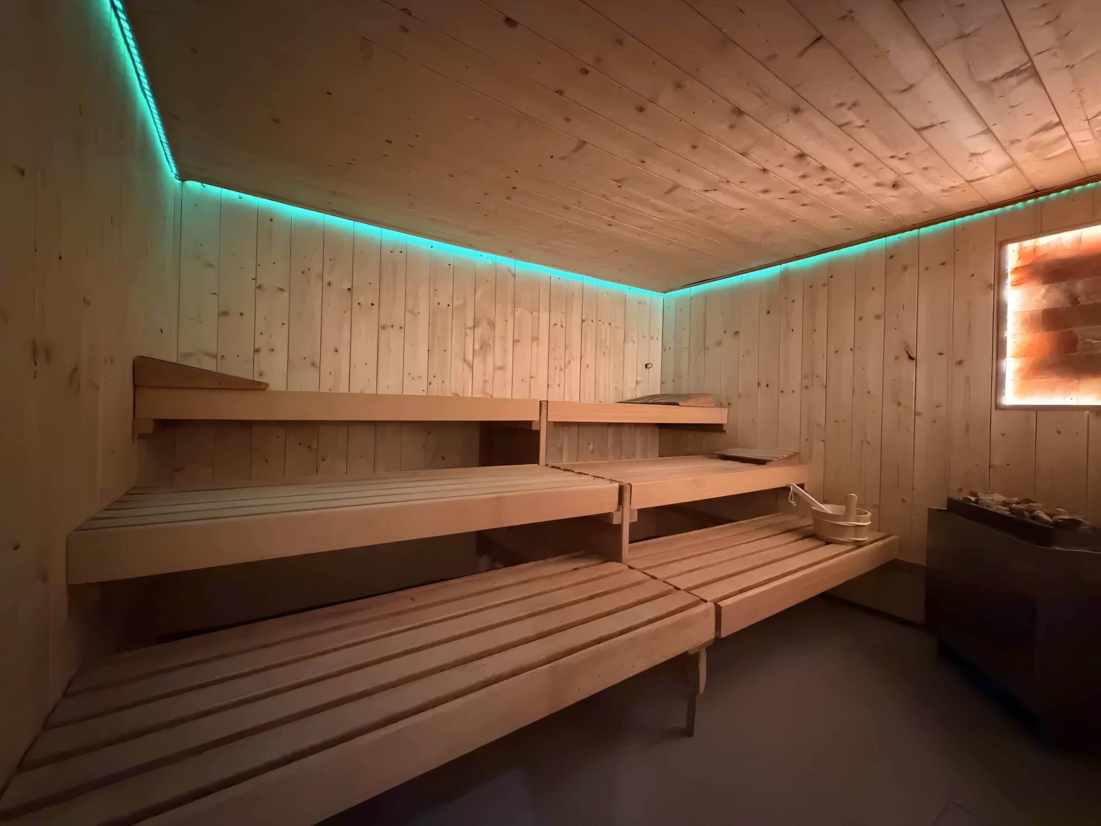 Una sala de sauna con bancos de madera y un asiento de banco, paredes de madera y otro asiento de banco.