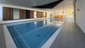 Moderni sisäuimahalli, jossa on laatoitettu lattia, puupaneloidut seinät ja kaltevaan muotoon suunniteltu katto.