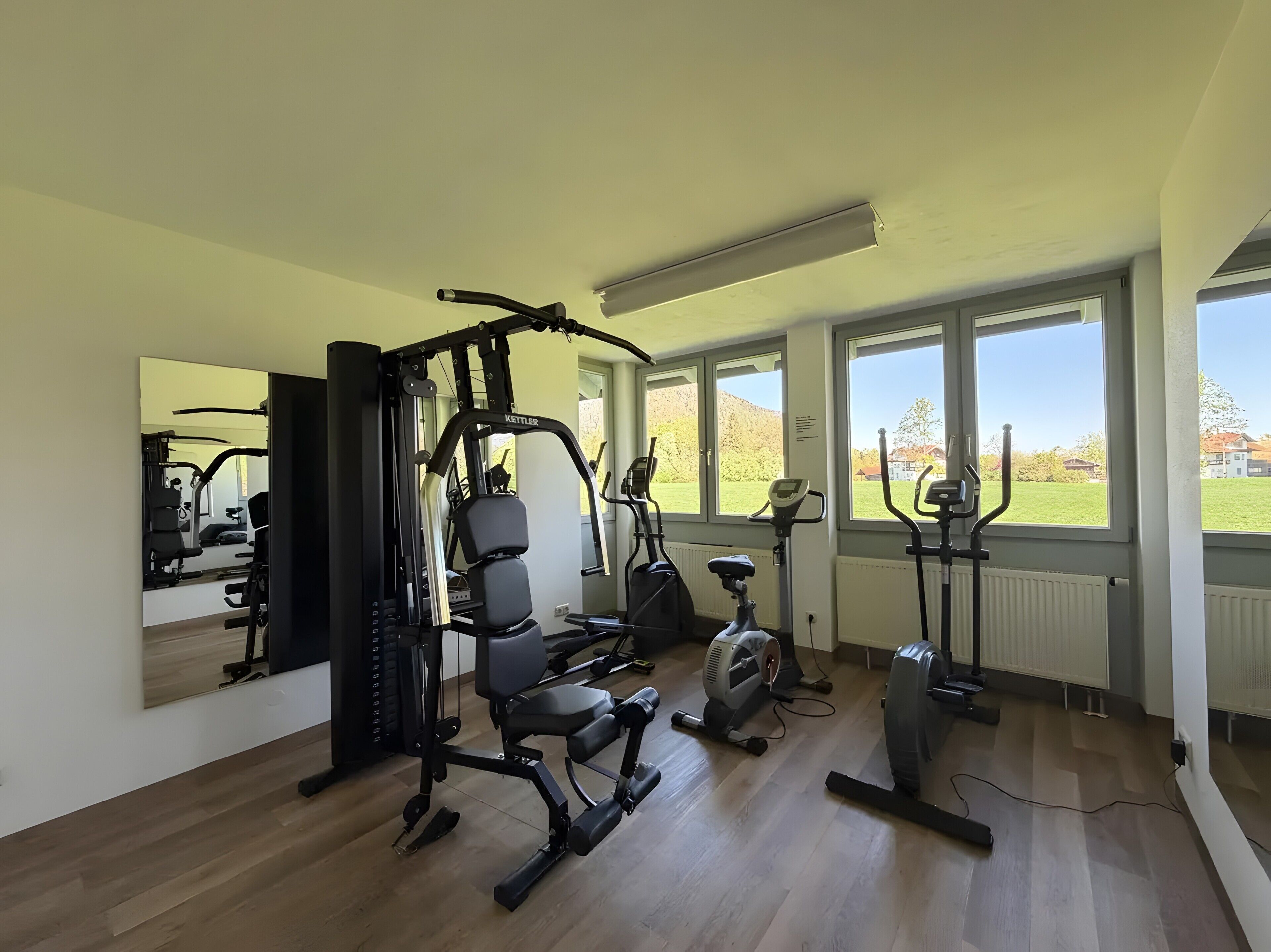 A gym with exercise equipment, large windows, and a view of a green landscape.
