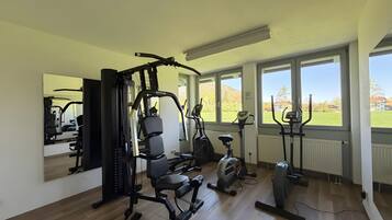 A gym with exercise equipment, large windows, and a view of a green landscape.