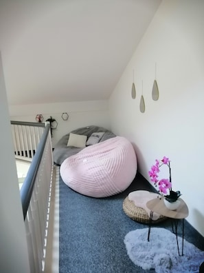 Une pièce avec un fauteuil poire gris, un fauteuil poire rose, une petite table ronde ornée d’une orchidée rose et un tapis blanc et moelleux.