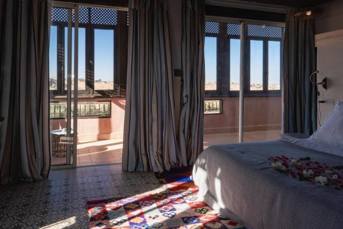Ein Schlafzimmer mit einem Bett, Vorhängen, Blick durch das Fenster und einem gemusterten Teppich.