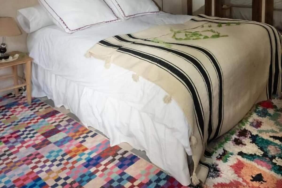 Ein Schlafzimmer mit Bett, Nachttisch, farbigem Teppich und Kleiderschrank.