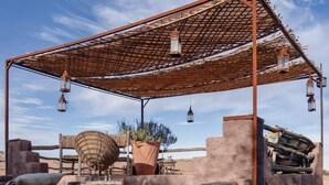 A rustic outdoor seating area with a metal pergola, lanterns, and a large potted plant. - Atlas Aura (Ourika)
