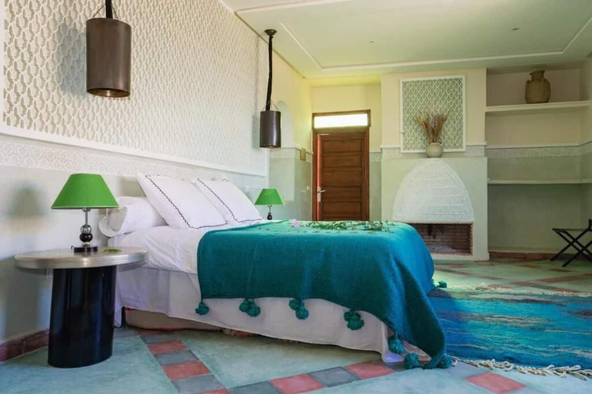 Ein Schlafzimmer mit einem Bett, zwei Nachttischen mit Lampen, einer Wand mit Muster, einem Kamin und einer Tür.