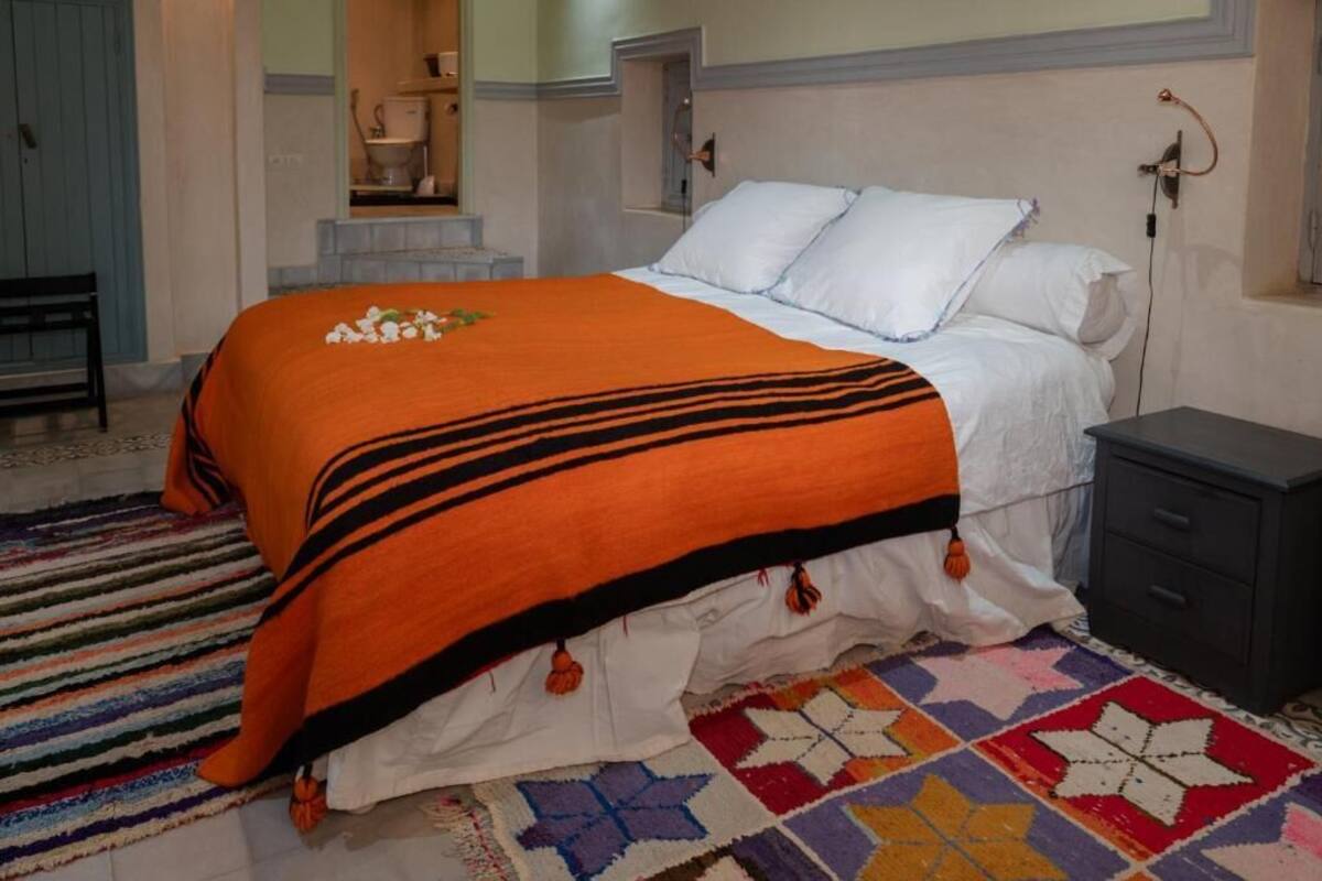Ein Schlafzimmer mit einem Bett, einem Nachttisch, einem Sessel, einem gemusterten Teppich und einer blauen Tür.