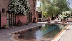 A swimming pool with a stone border, surrounded by potted plants and outdoor furniture. - Atlas Aura (Ourika)