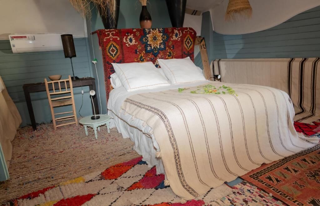 Un dormitorio con cama, mesita de noche, silla, alfombra y aire acondicionado instalado en la pared.