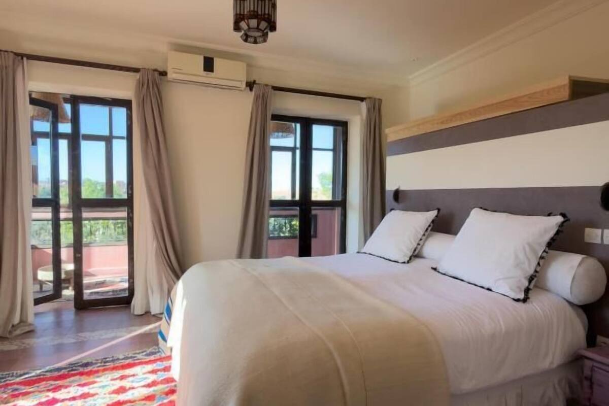 Ein geräumiges Schlafzimmer mit einem großen Bett, einem gemusterten Teppich und Blick ins Freie durch eine Schiebetür.