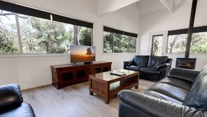 Un salon moderne avec une cheminée, des canapés en cuir, une table basse en bois et un téléviseur posé sur un meuble en bois.