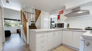 Une cuisine moderne avec des meubles blancs, un four à micro-ondes, une cuisinière et un escalier en bois.