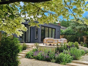 A modern house with a patio, outdoor seating, and a garden with various plants. - Fairview (Saxmundham)