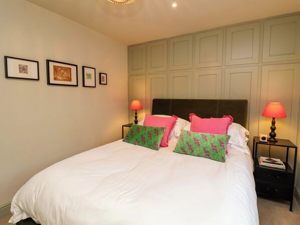 A neatly made bed with white linens and decorative pillows, two bedside lamps, and framed artwork on the wall. - Fairview (Saxmundham)