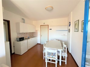Cocina compacta con armarios blancos, un lavamanos y un microondas. Hay una mesa de comedor con sillas en el centro de la habitación.