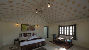 Une chambre spacieuse avec un grand lit, un bureau et une chaise, un ventilateur de plafond et une fenêtre avec des rideaux.