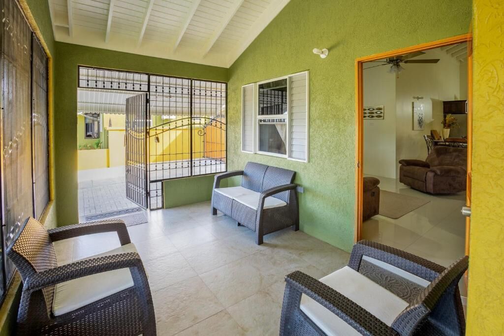 A room with wicker furniture, a window with blinds, a door leading to another room, and a tiled floor.