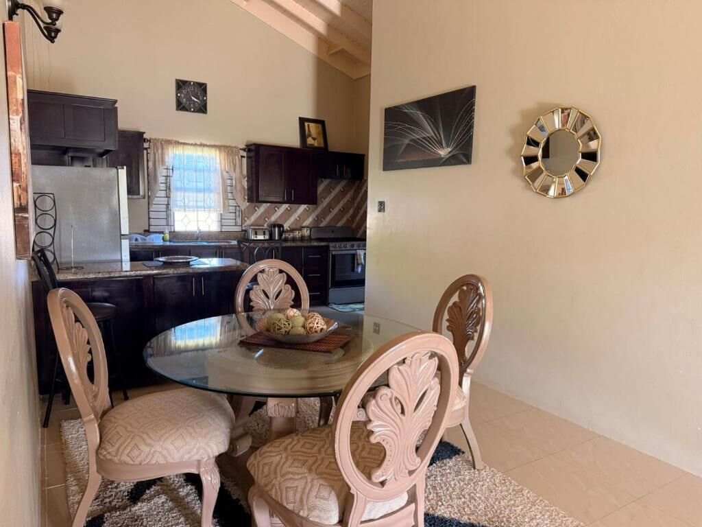 A dining area with a round table and four chairs, a kitchen in the background, and decorative wall art.