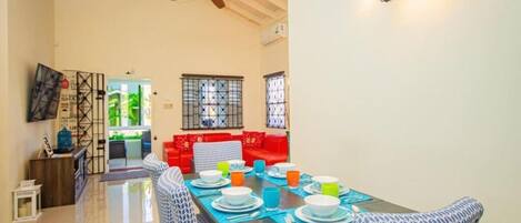 A dining area with a table set for four, a ceiling fan, and a red sofa in the background.