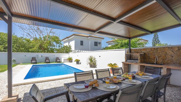 Ett utomhusområde med plats för måltider, en pool, en grill och utsikt över ett vitt hus.