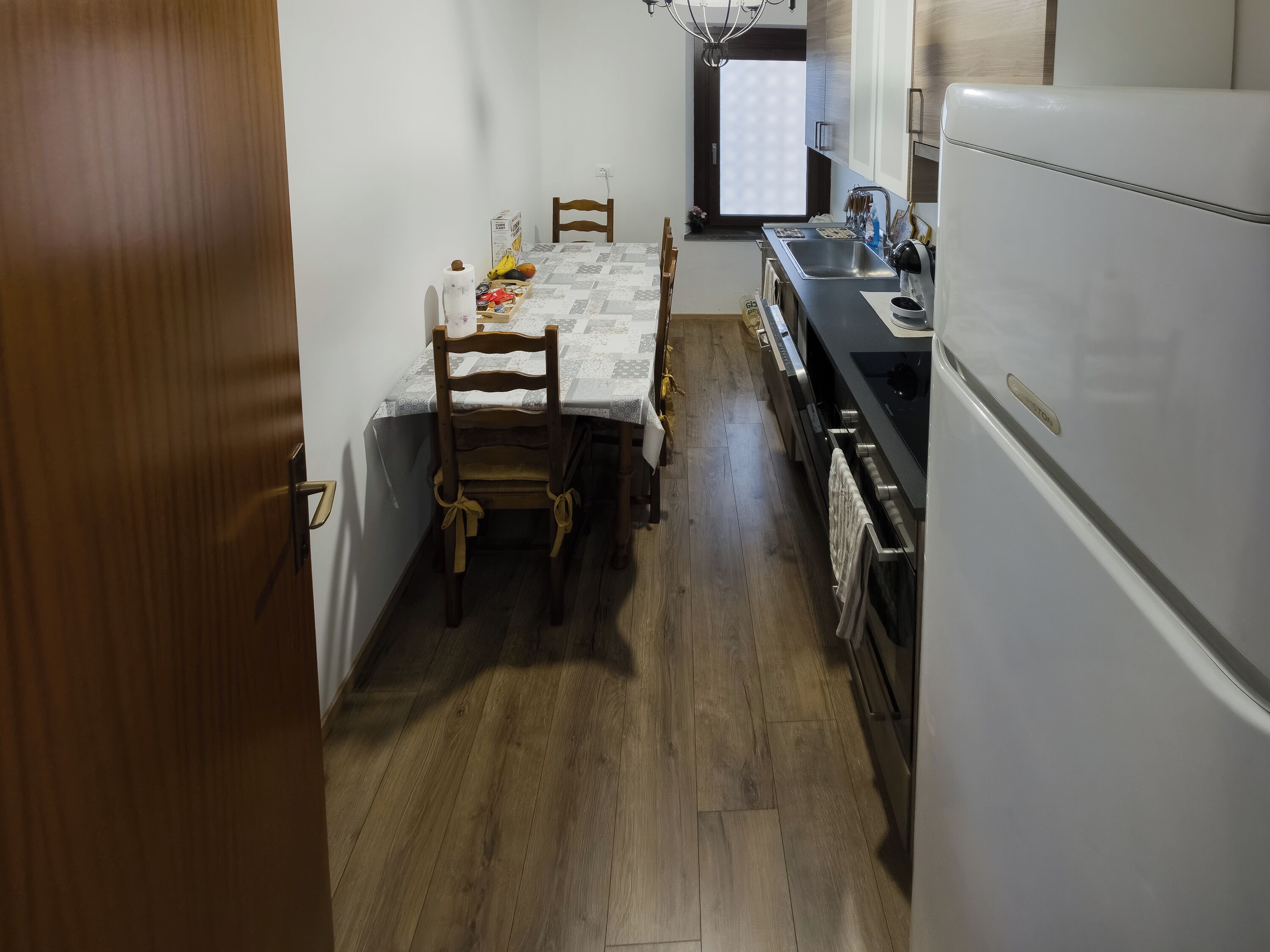 A compact kitchen with a dining table, chairs, a refrigerator, and a window.