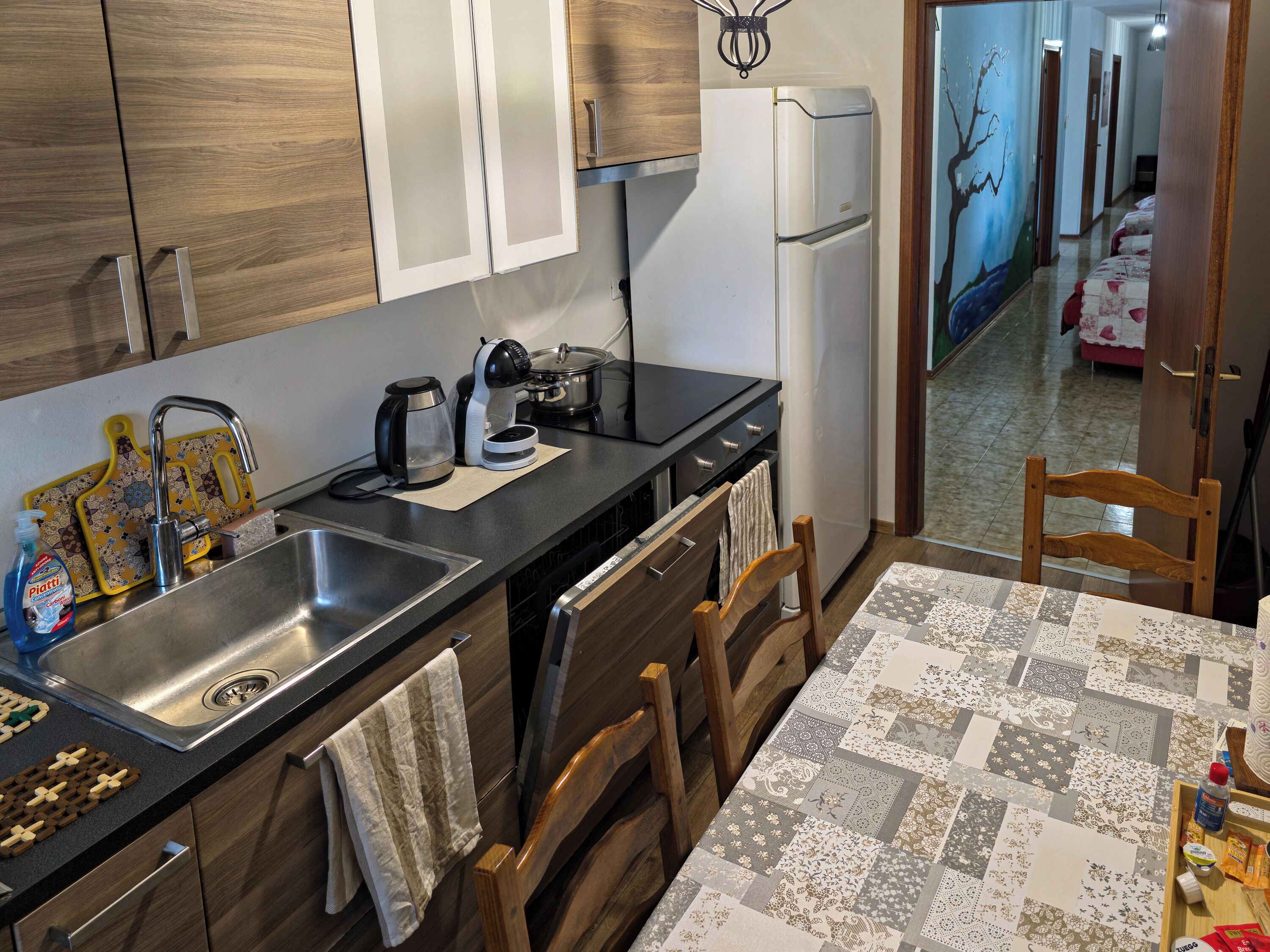 A modern kitchen with a stainless steel sink, a coffee maker, and a refrigerator.