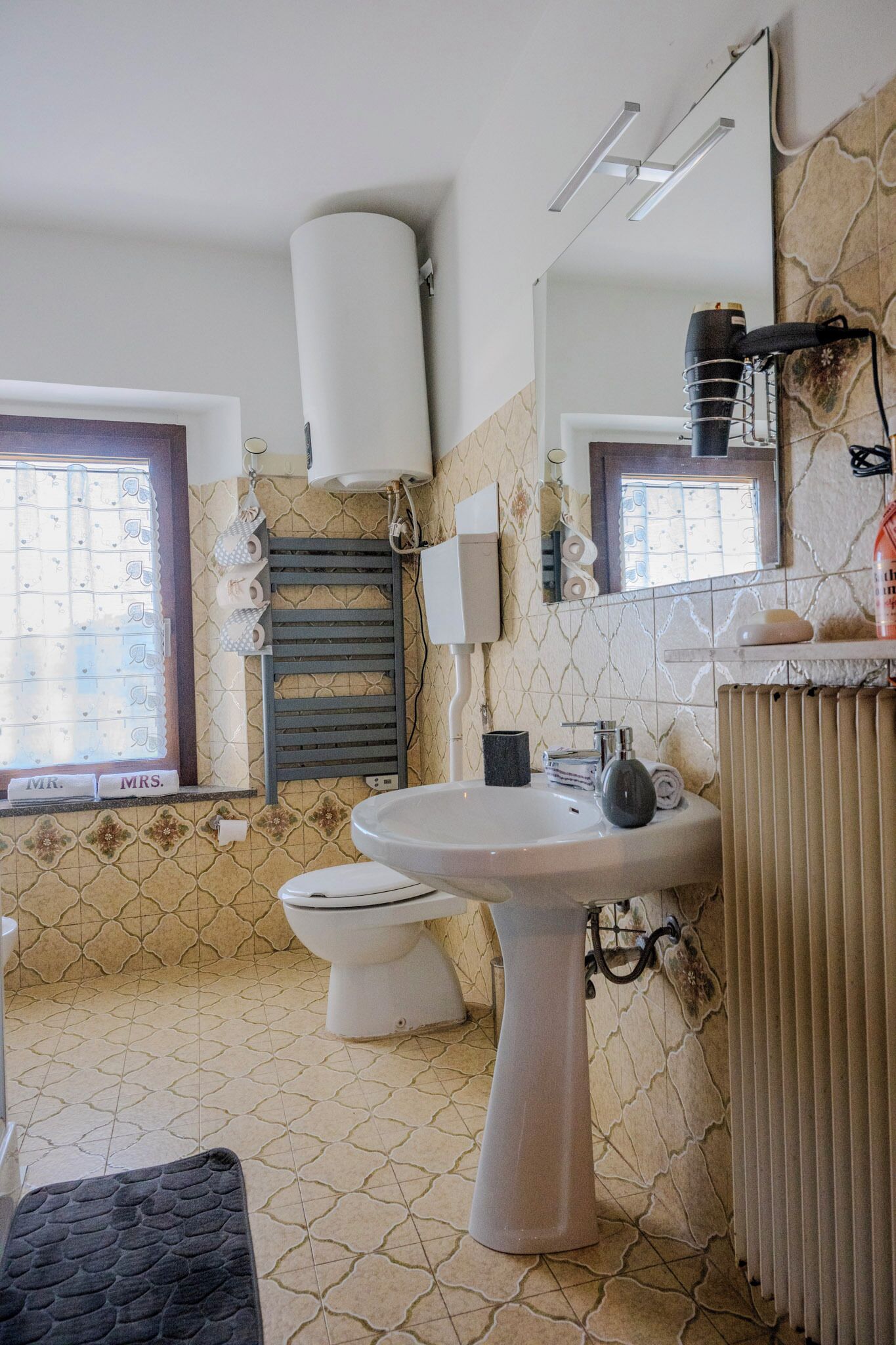 A bathroom with a toilet, sink, towel rack, and a radiator.