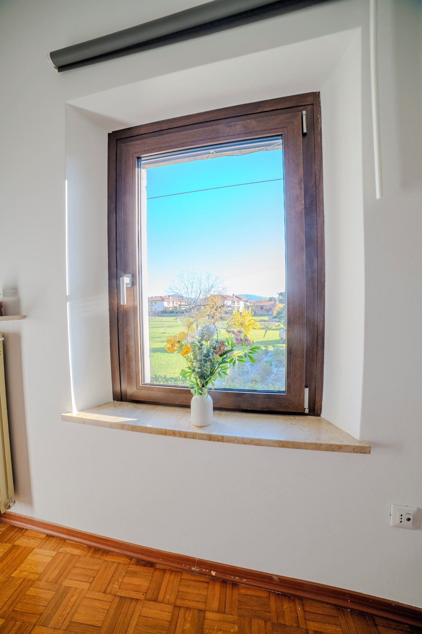 Una habitación con ventana, con marco de madera y una pequeña estantería debajo.