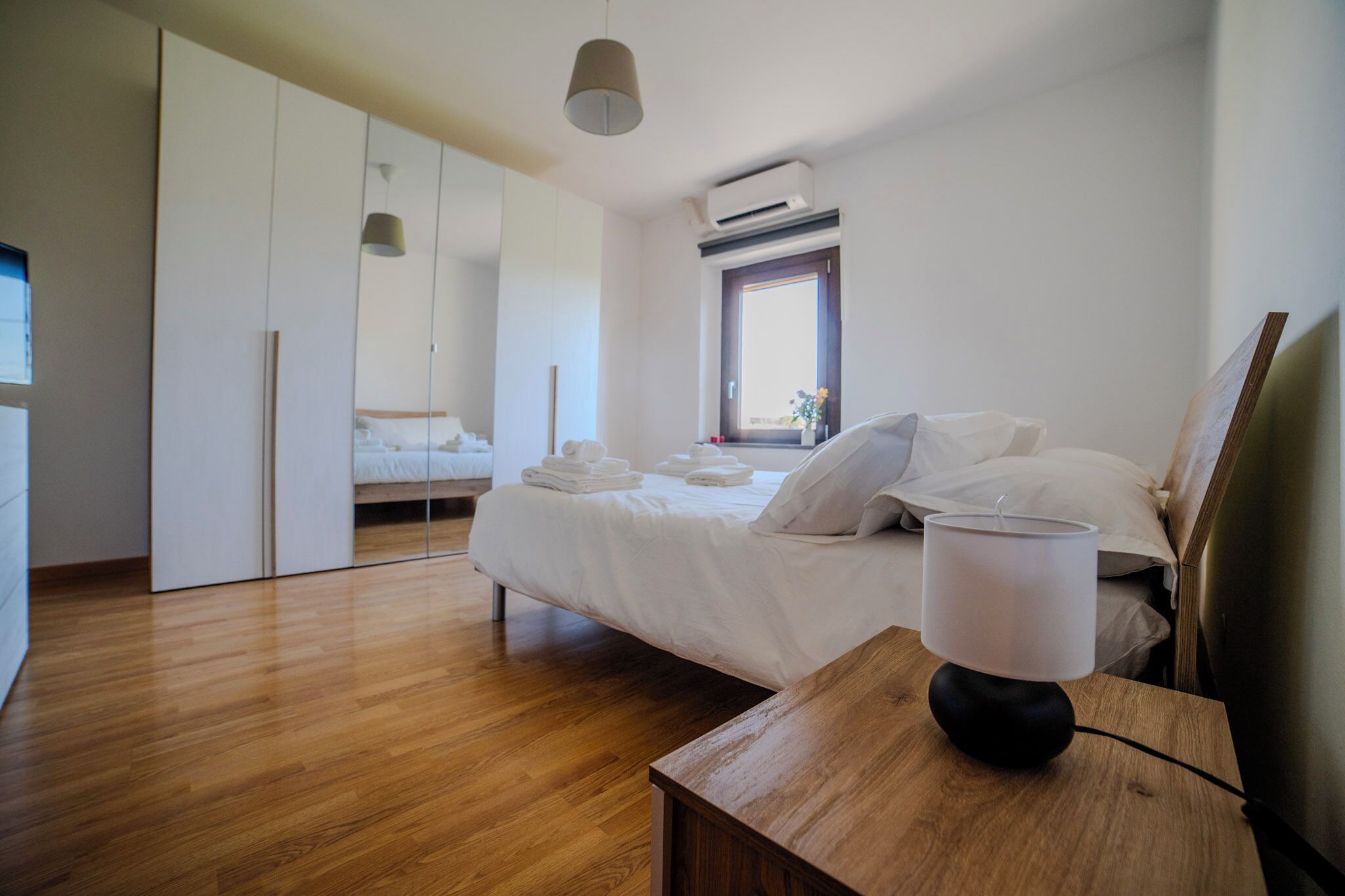 Ein modernes Schlafzimmer mit Holzboden, einem Bett mit weißen Leinentüchern, einem Nachttisch mit Lampe und einem Kleiderschrank.