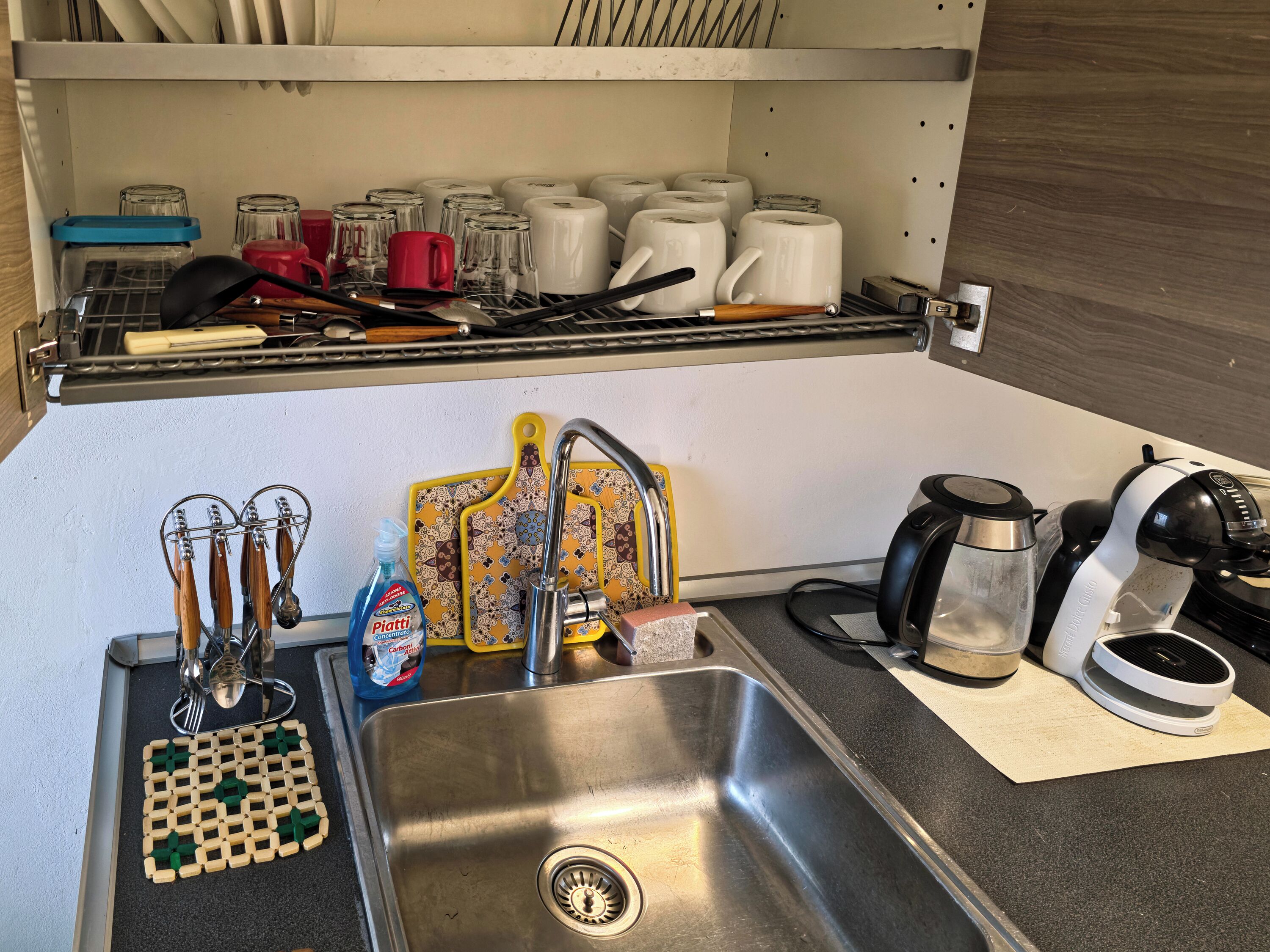 A kitchen with a stainless steel sink, a coffee maker, and various utensils.