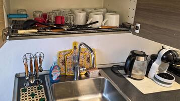 A kitchen with a stainless steel sink, a coffee maker, and various utensils.