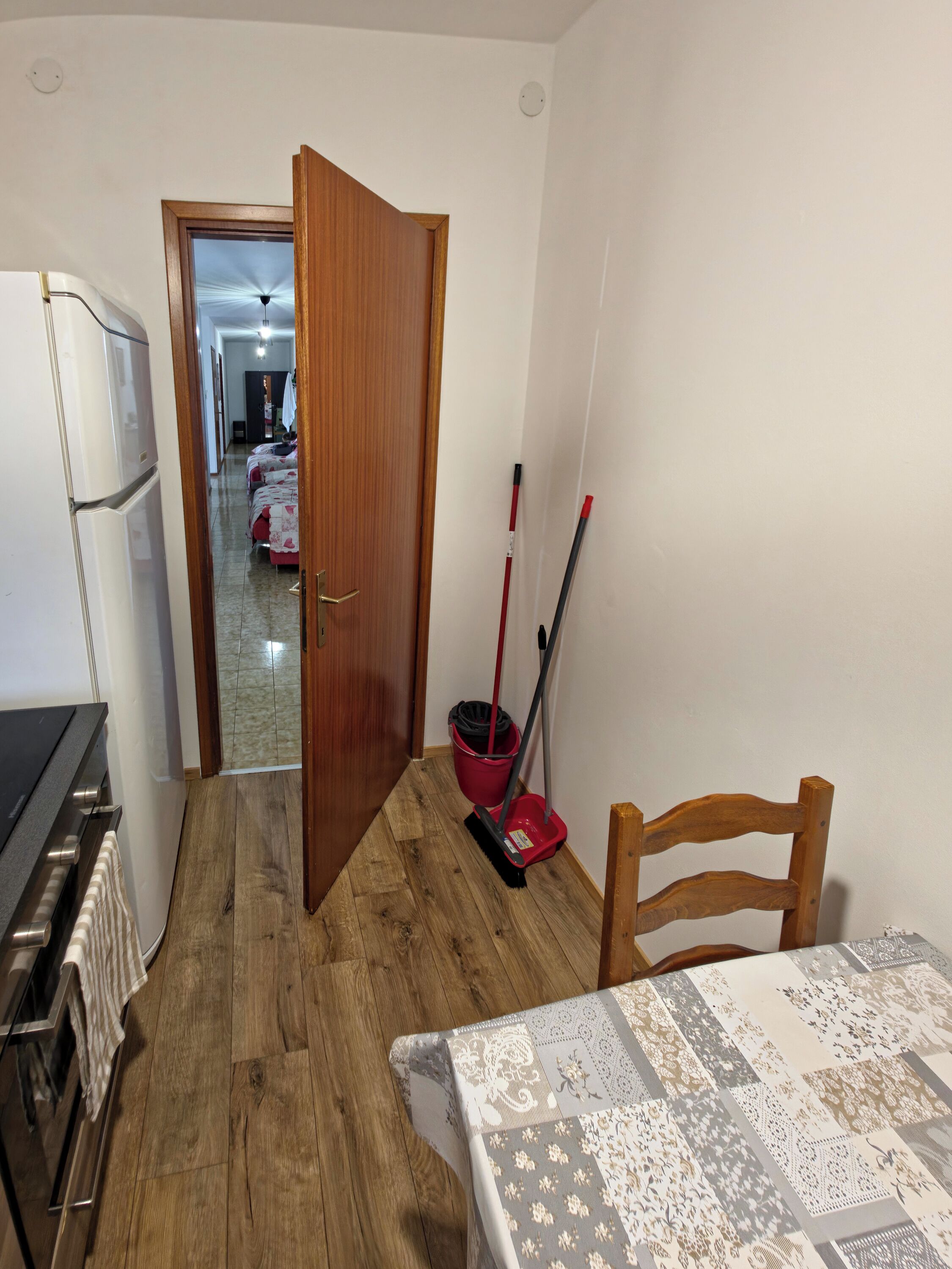 Ein Zimmer mit Holzboden, einem Esstisch mit gemustertem Tischläufer, einem roten Mop und einem Holzstuhl.