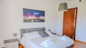 A neatly made bed with white linens and towels, a gray headboard, a bedside table with a lamp, and a cityscape painting on the wall. - Dimora del 700' (Premariacco)