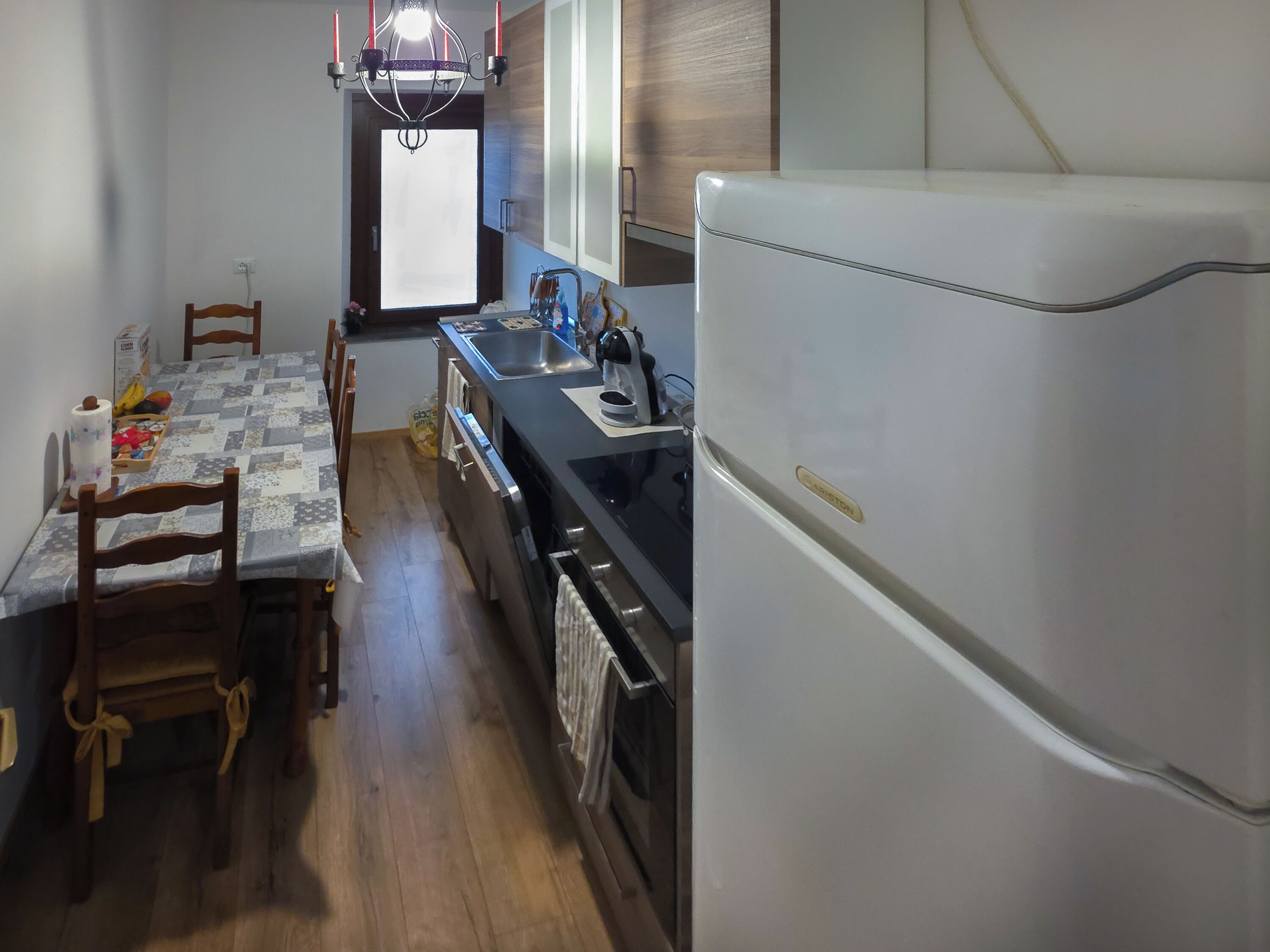 A compact kitchen with a refrigerator, stove, sink, and wooden dining table with chairs.