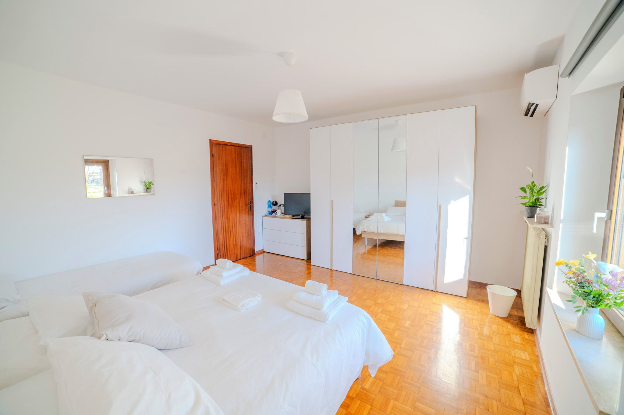 A modern bedroom with a large bed, a wardrobe, a desk, and a mirror.