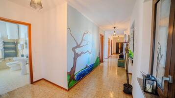 A hallway with a painting of a tree and river, a sink, toilet, and a potted plant.