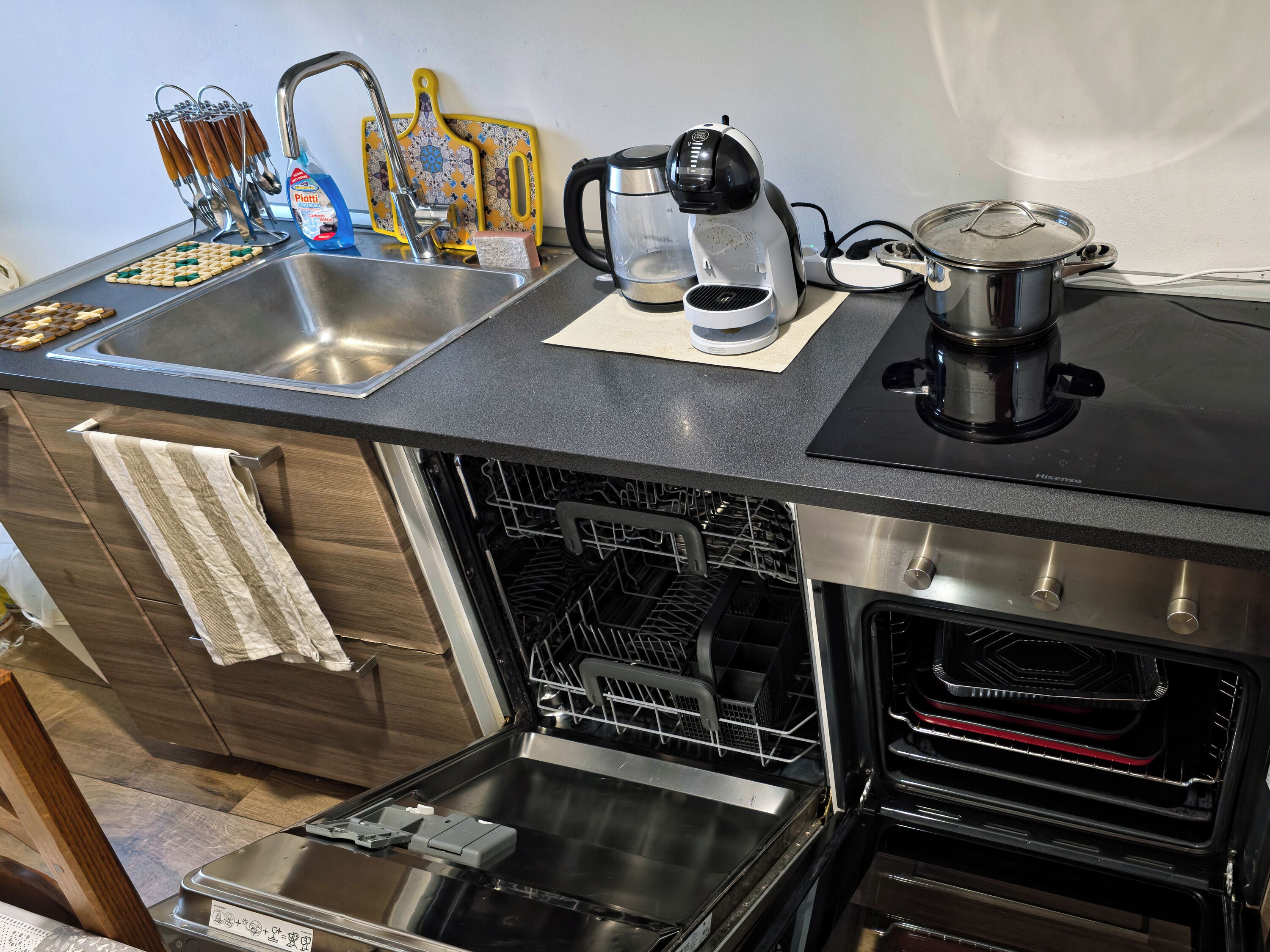 A compact kitchen with a sink, a coffee maker, a kettle, and a stove.