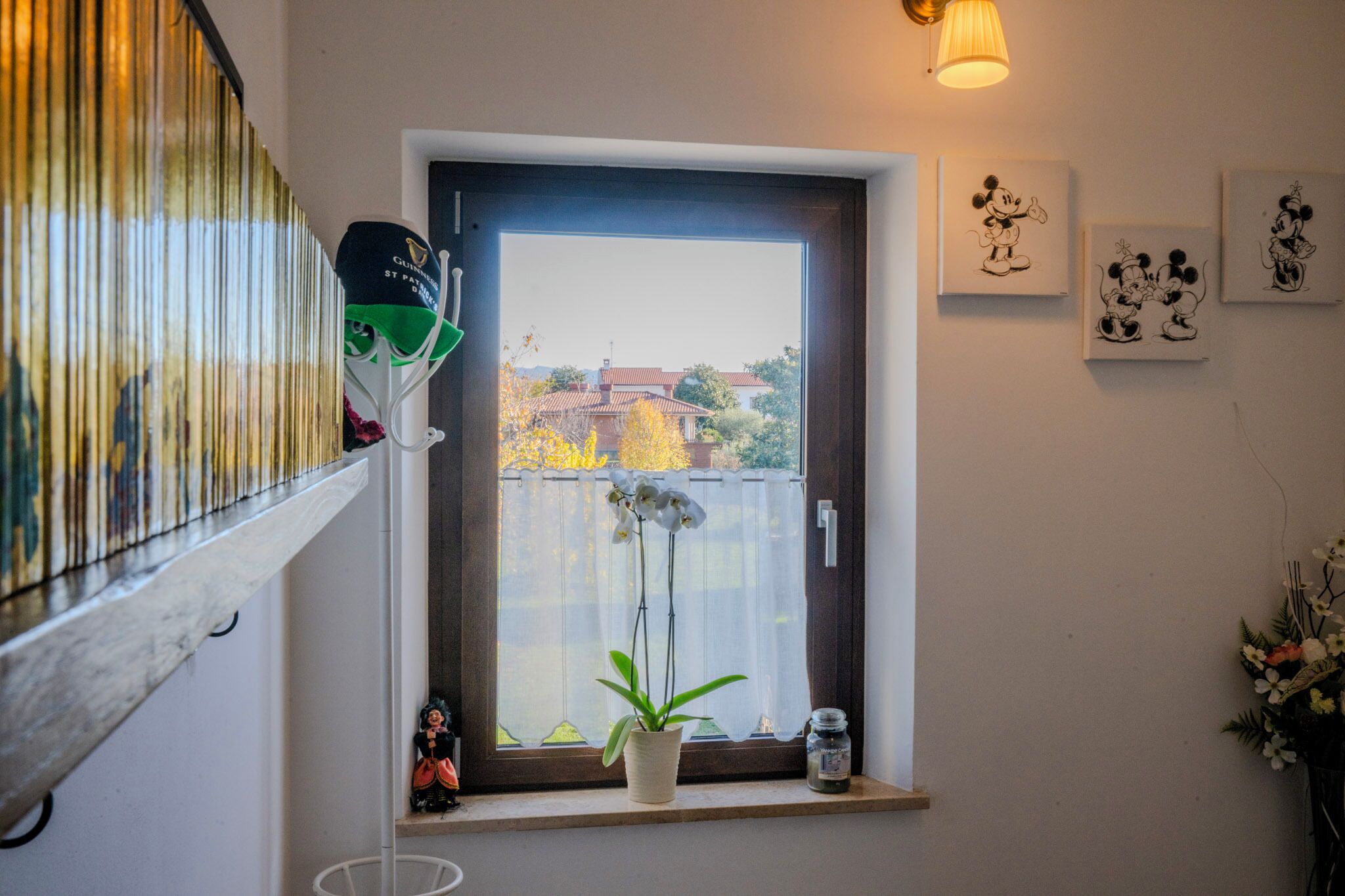A room with a window, a potted plant, a small shelf with a bag and a bottle, and wall art.