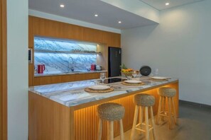 A modern kitchen with a marble countertop, wooden accents, and bar stools. - Villa Talun by GORO (Kabupaten Gianyar)