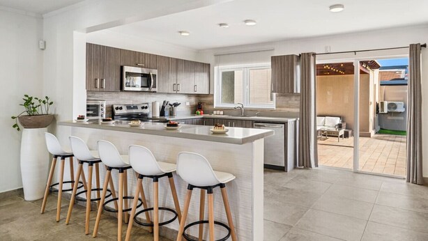 Een moderne keuken met een centraal eiland, barstoelen en een eethoek met uitzicht naar buiten.