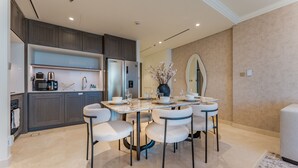 A modern kitchen with dark wood cabinets, a built-in oven, and a dining area with a marble table and white chairs. - Direct Private Beach Access, Proximity To Key Dubai Attractions Like Dubai Marina, Palm Jumeirah (Dubai)