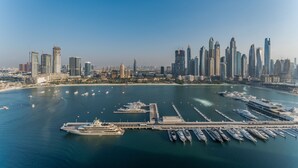 A marina with numerous yachts docked, a large cruise ship, and a city skyline with modern skyscrapers in the background. - Direct Private Beach Access, Proximity To Key Dubai Attractions Like Dubai Marina, Palm Jumeirah (Dubai)